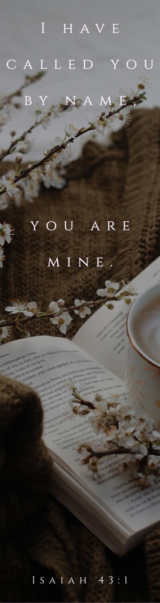 Bookmark reading I have called you by name, you are mine, in letterspaced serif over an open book, a cup of coffee and blossom on a knitted blanket